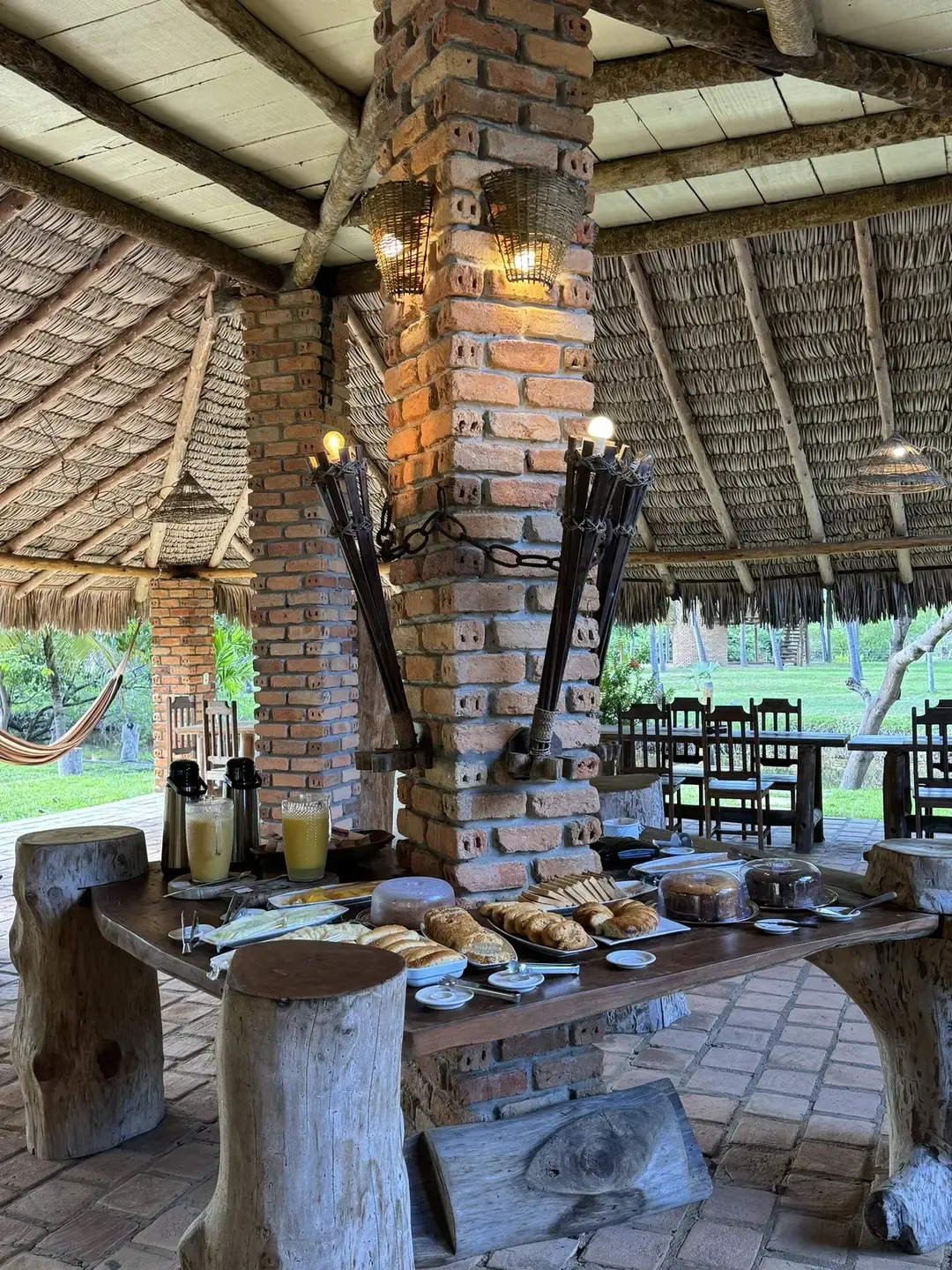 Mesa do café da manhã com pães e bolos caseiros, sob o telhado de palha