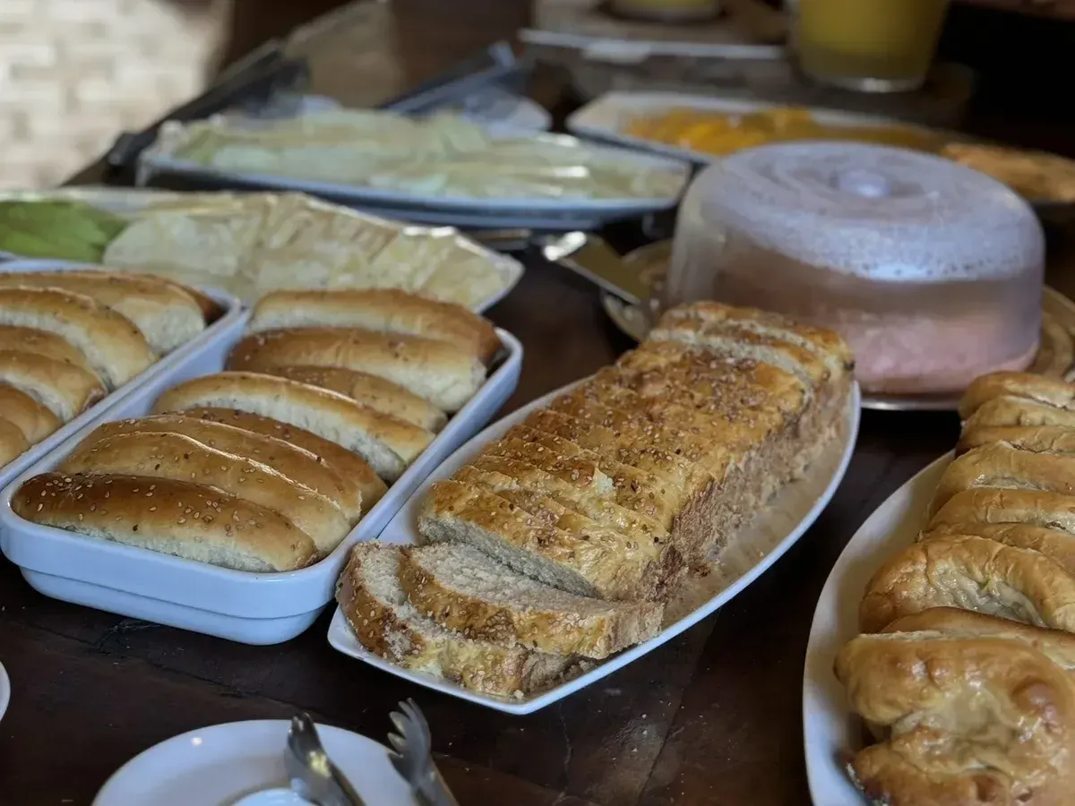 Pães caseiros, bolo e sucos na mesa do café da manhã