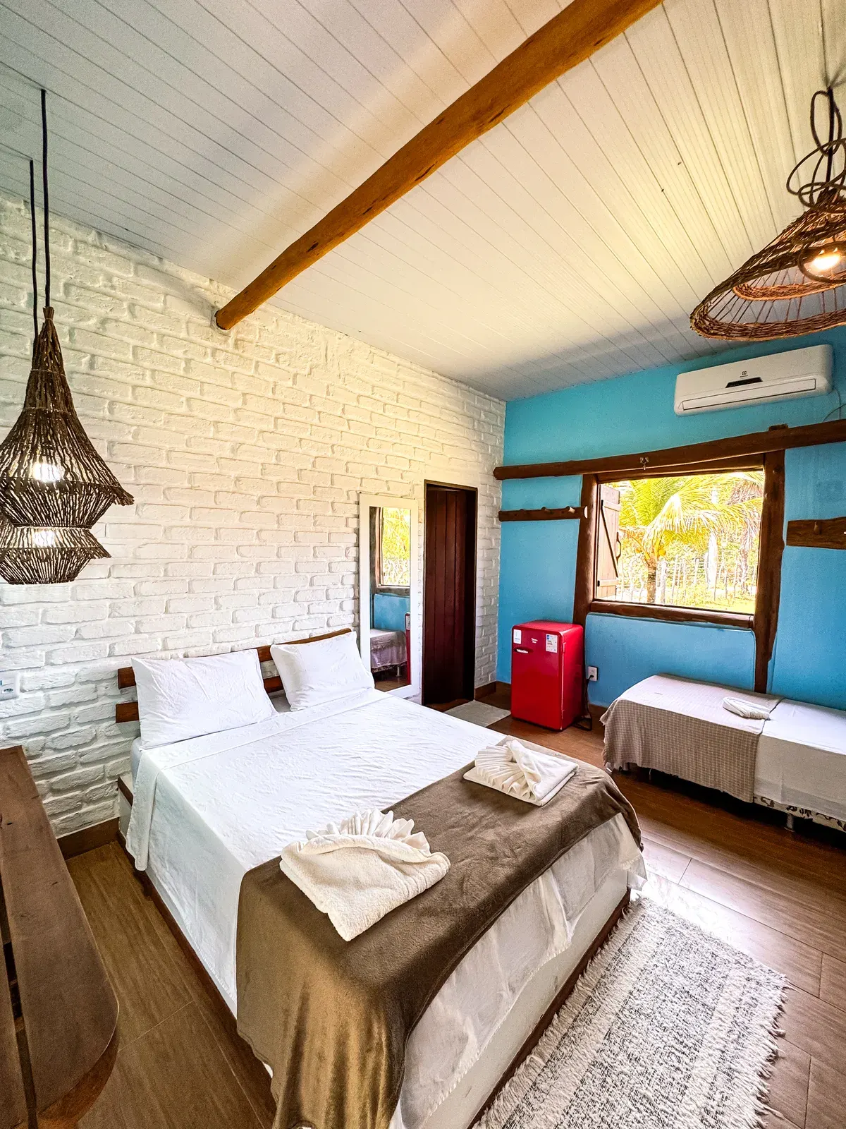 Cama de casal e cama de solteiro no Bungalow Família, com parede de tijolo branco, parede azul e janela de madeira