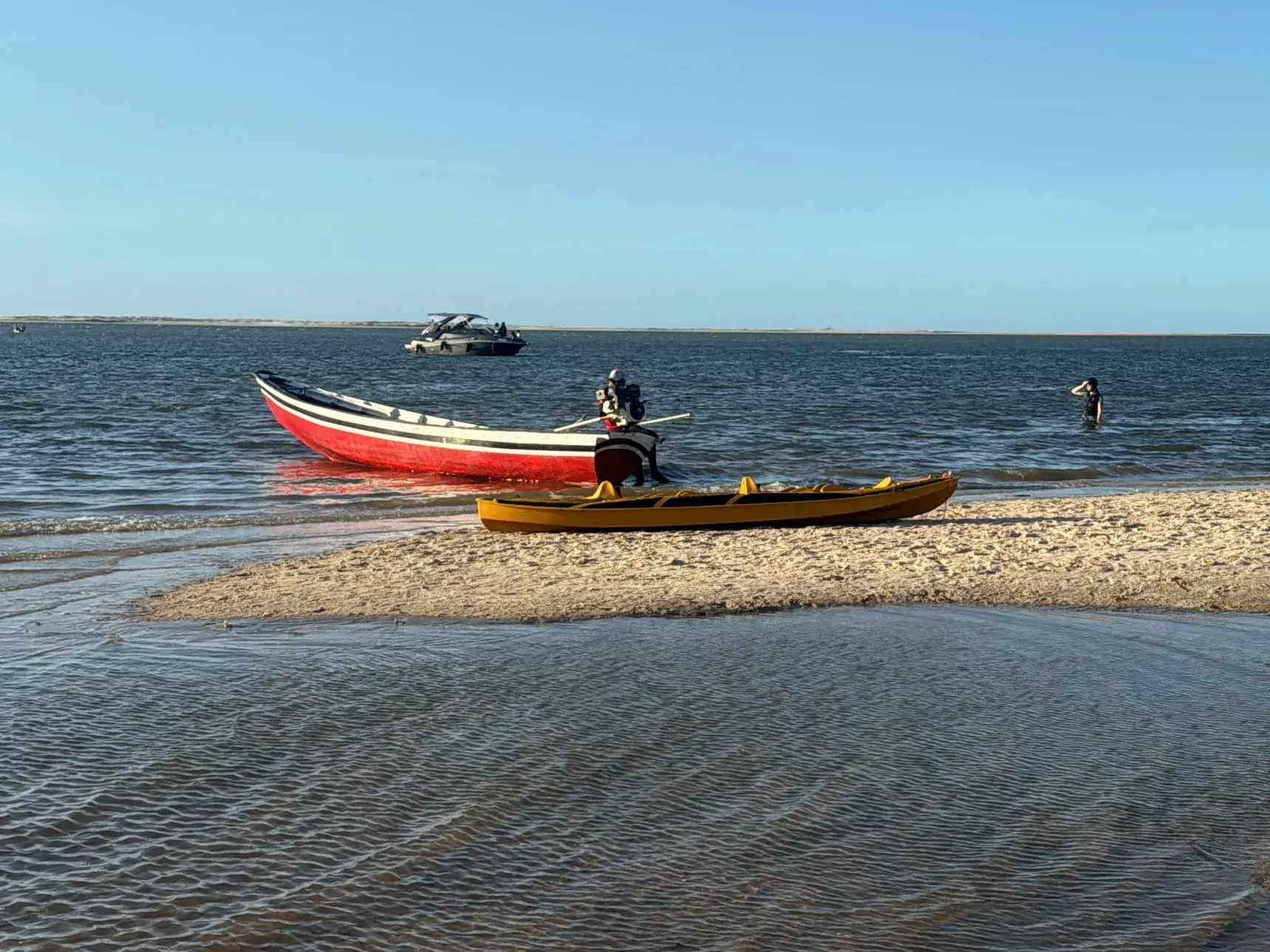 Um barco vermelho e um caiaque amarelo num banco de areia, à beira d’água